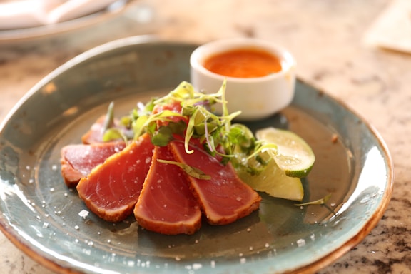 A beautifully plated dish of tataki tuna with citrus emulsion and sesame crisp on a rustic wooden table.