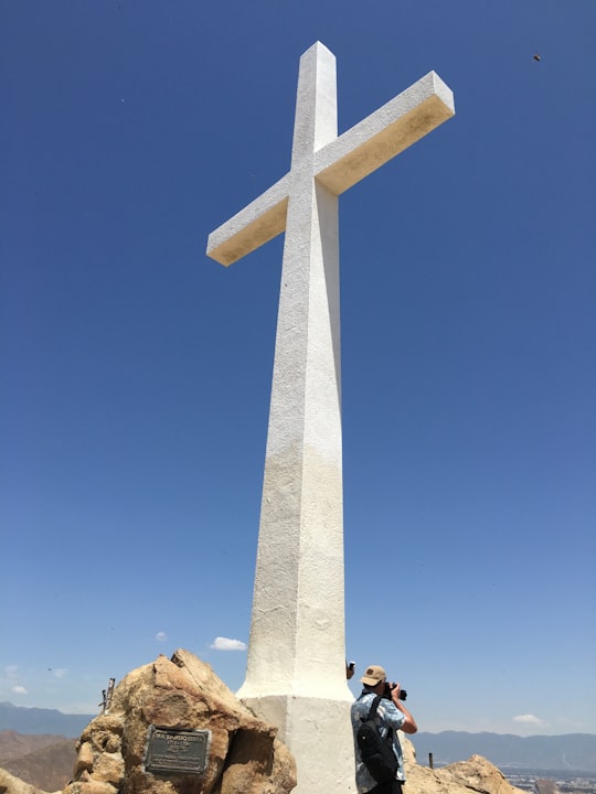 person in blue top using DSLR camera under white concrete cross in Mount Rubidoux Park United States