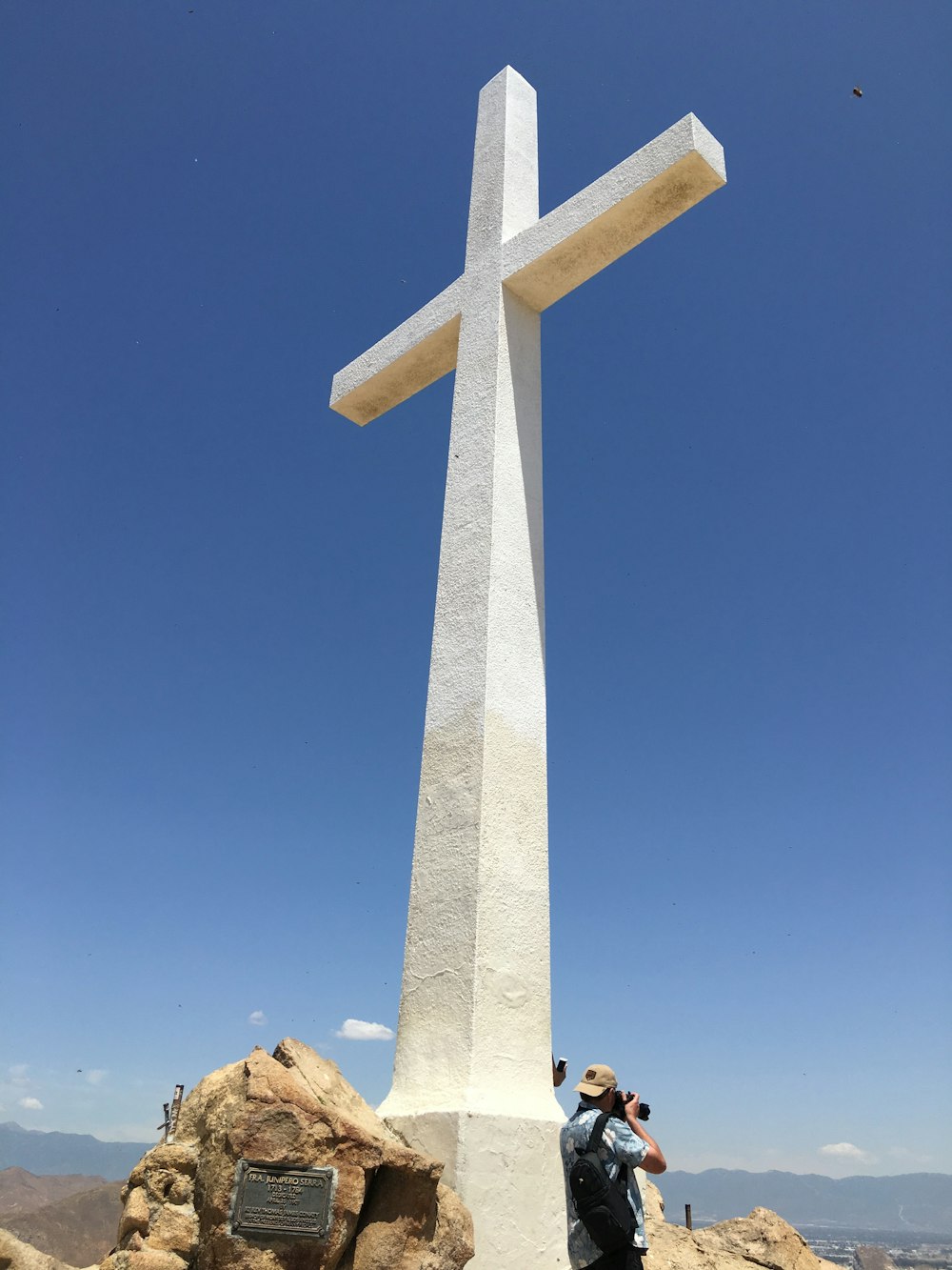 person in blue top using DSLR camera under white concrete cross