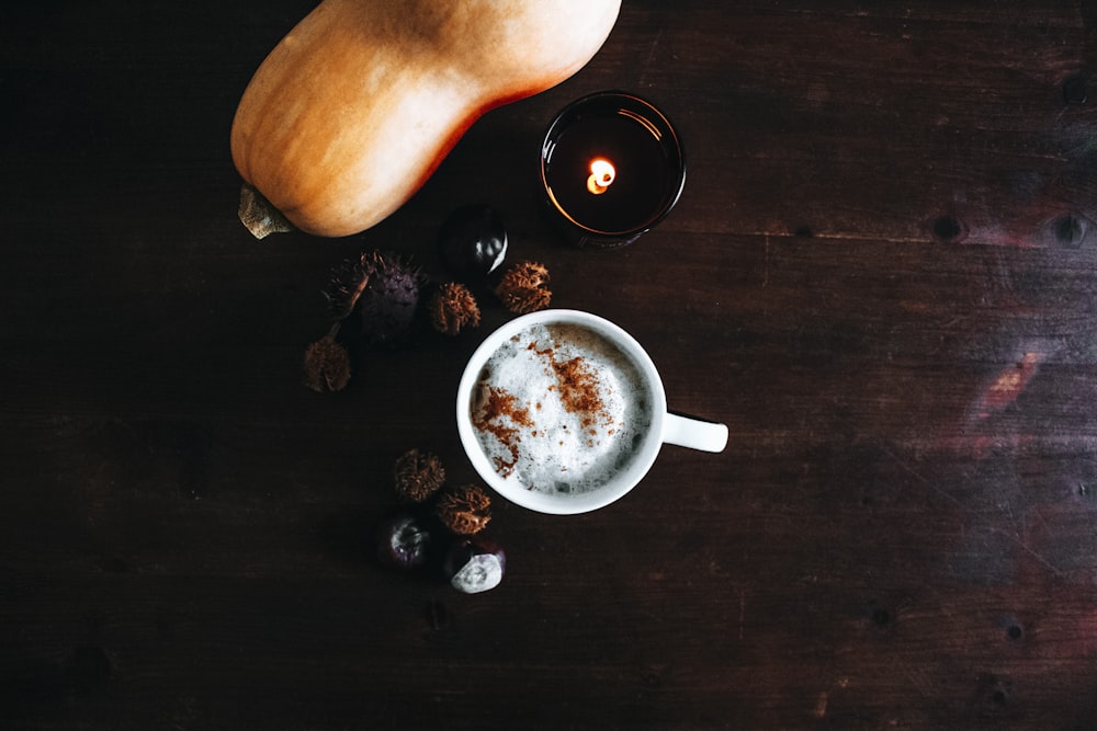 xícara de café perto do vegetal alaranjado na superfície de madeira marrom