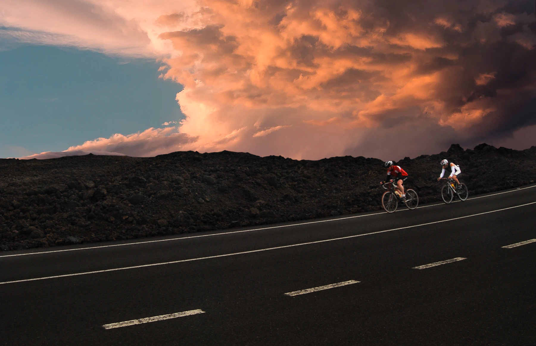 Two cyclists riding a dramatic mountain road at golden hour