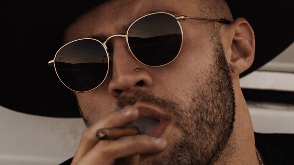 Close up of a man in a hat and sunglasses smoking a cigarello