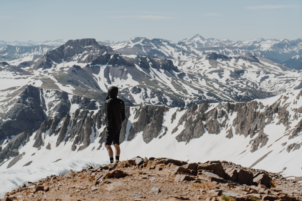 uomo che indossa pantaloncini neri in piedi sulla formazione rocciosa di fronte alla montagna