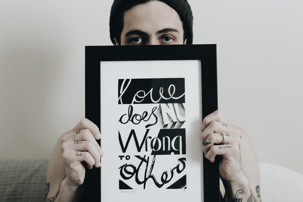 A person holding a picture frame with writing inside that says "Love does no wrong to others."