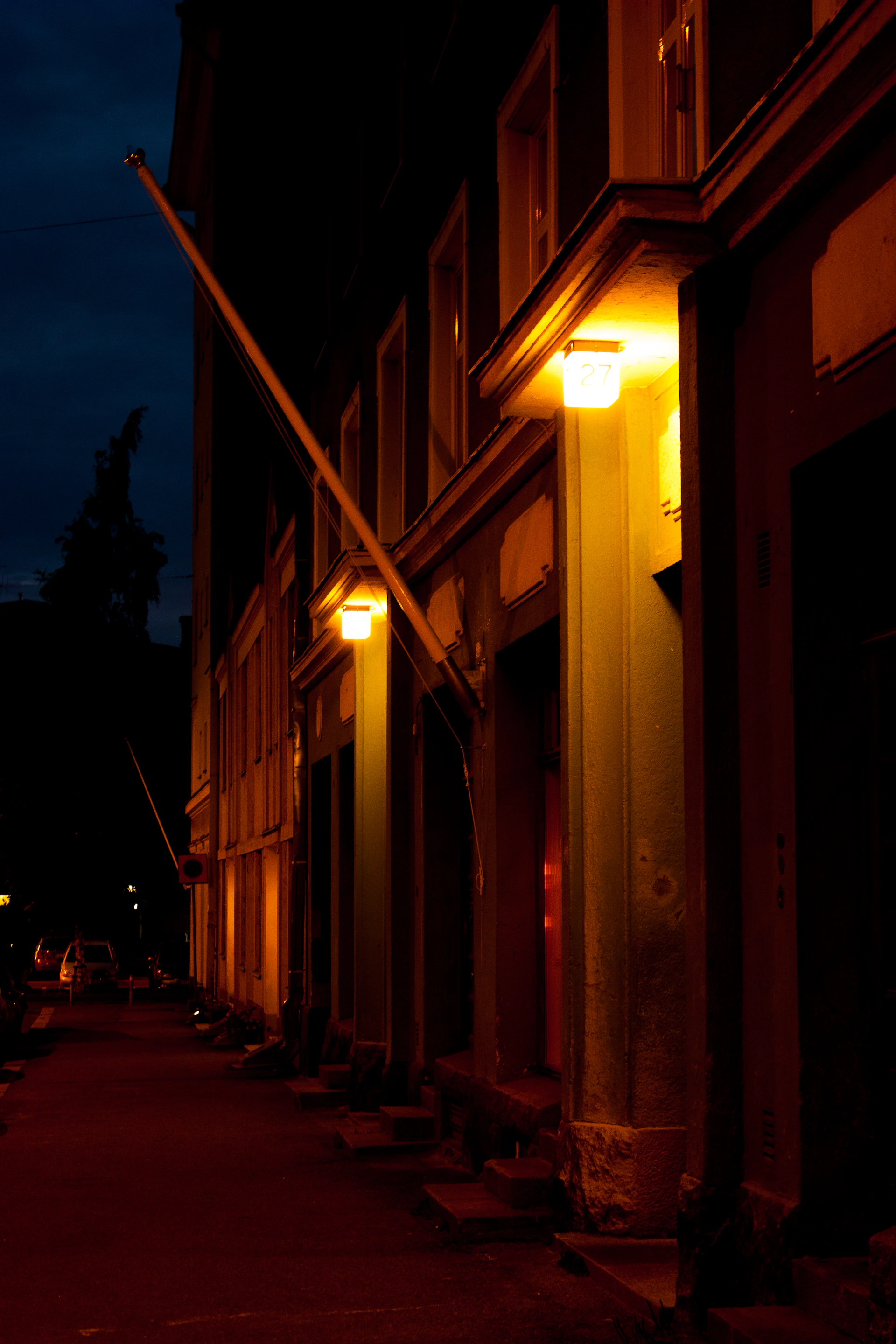 An urban street scene at dusk, with soft lights glowing from windows and subtle shadows on the pavement.