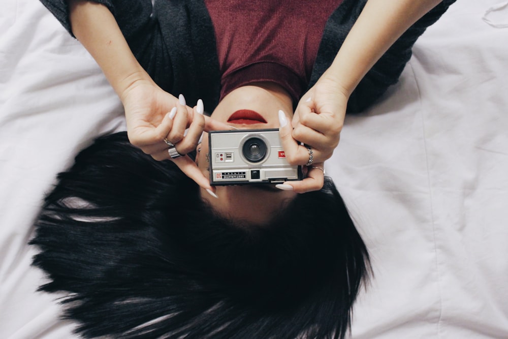 femme couchée dans un haut rouge et noir tenant un appareil photo argenté