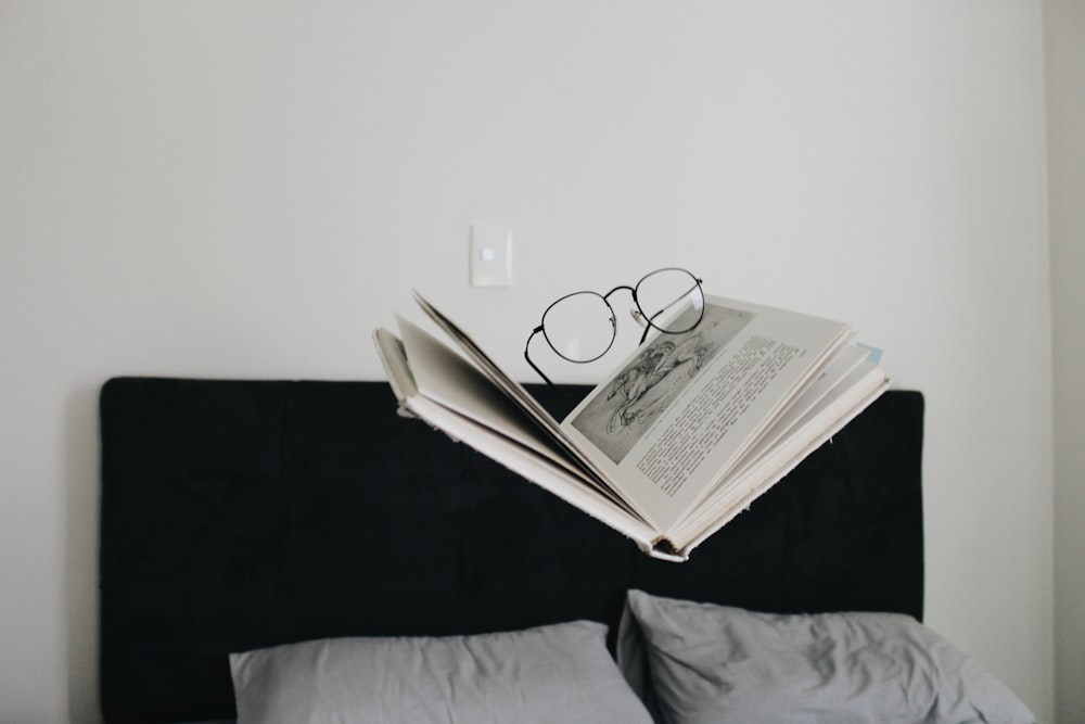 eyeglasses on top of book above bed