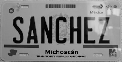 A black and white license plate from Michoacán, Mexico, displaying the name 'SANCHEZ' in bold letters. The plate includes a map outline of the region and text reading 'Transporte Privado Automovil'. Various official symbols and serial numbers are visible.