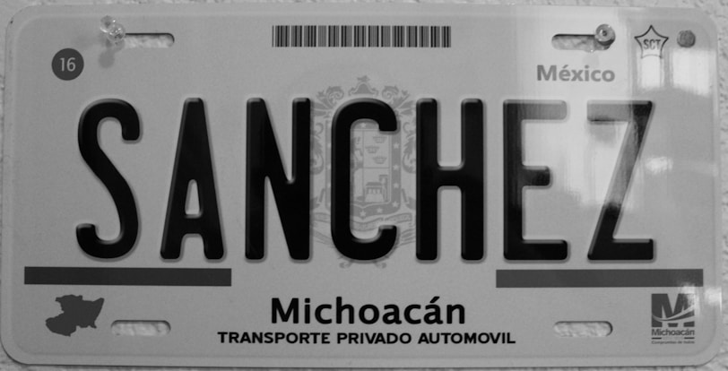A black and white license plate from Michoacán, Mexico, displaying the name 'SANCHEZ' in bold letters. The plate includes a map outline of the region and text reading 'Transporte Privado Automovil'. Various official symbols and serial numbers are visible.