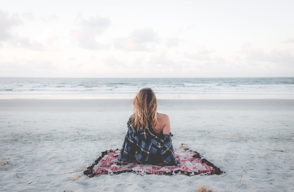 海岸線にある毛布の上に座っている女性