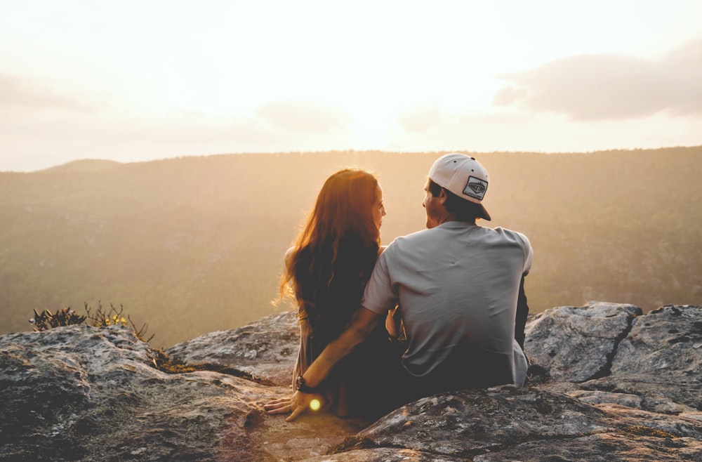 uomo e donna che si siedono sulla roccia durante il giorno