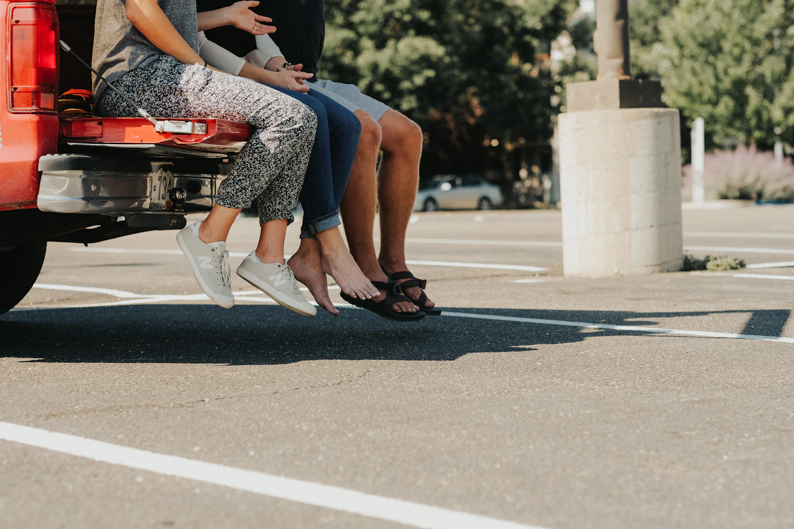People sitting on the open tailgate of a pickup truck in a sunny parking lot