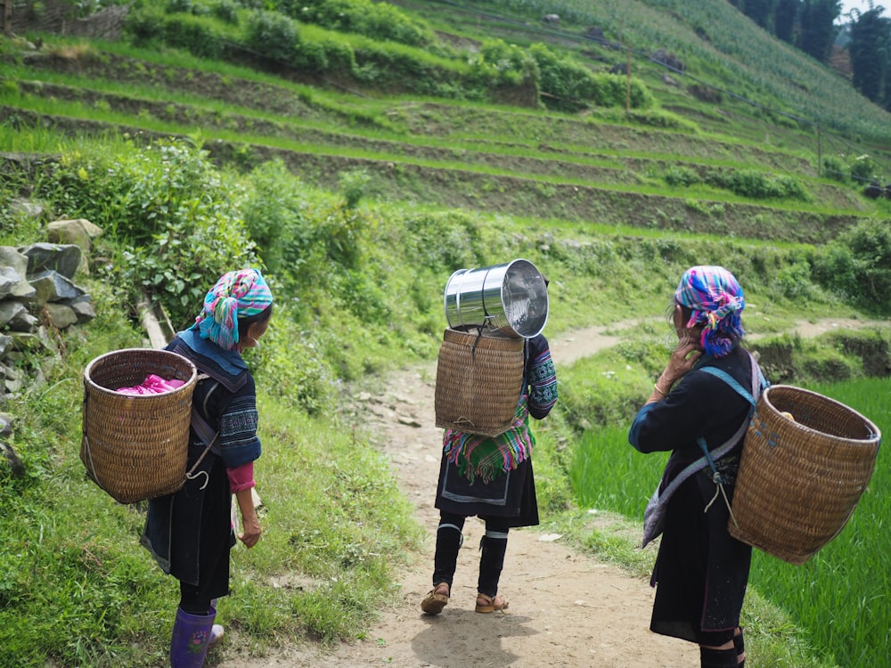 three people wearing brown wicker baskets walking on road