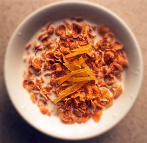 A bowl filled with milk and cornflakes, topped with thin slices of dried fruit, creating a visually appealing and nutritious breakfast setting.