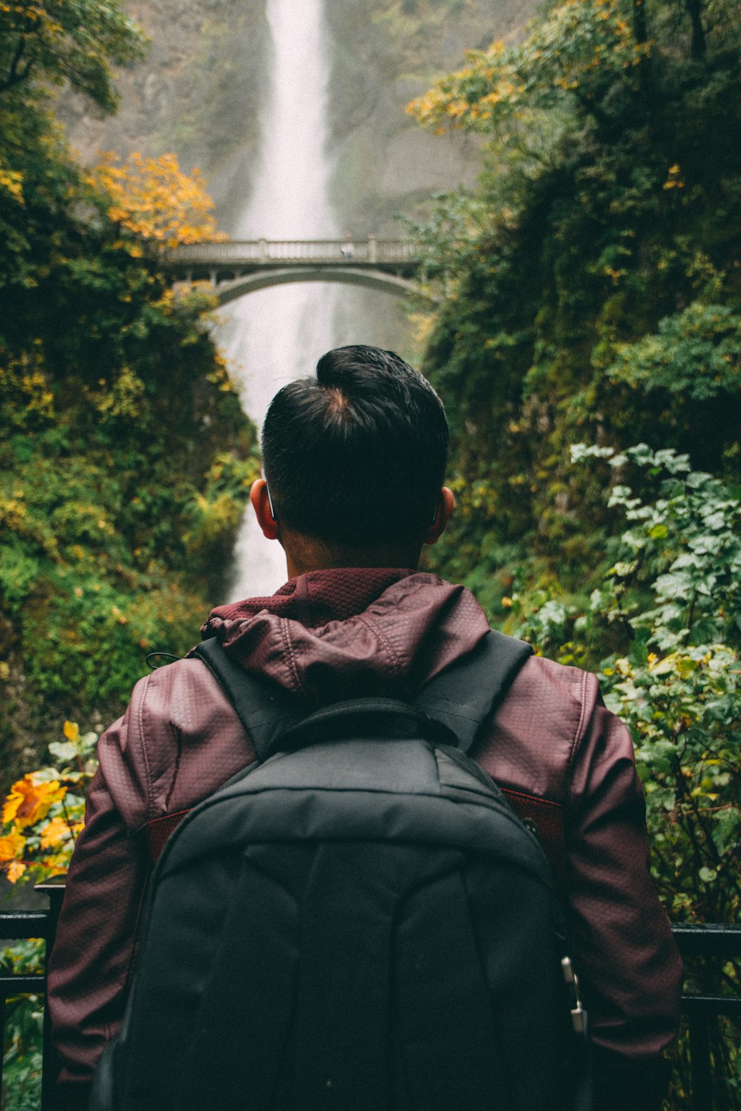 man looking up the bridge near the waterfalls