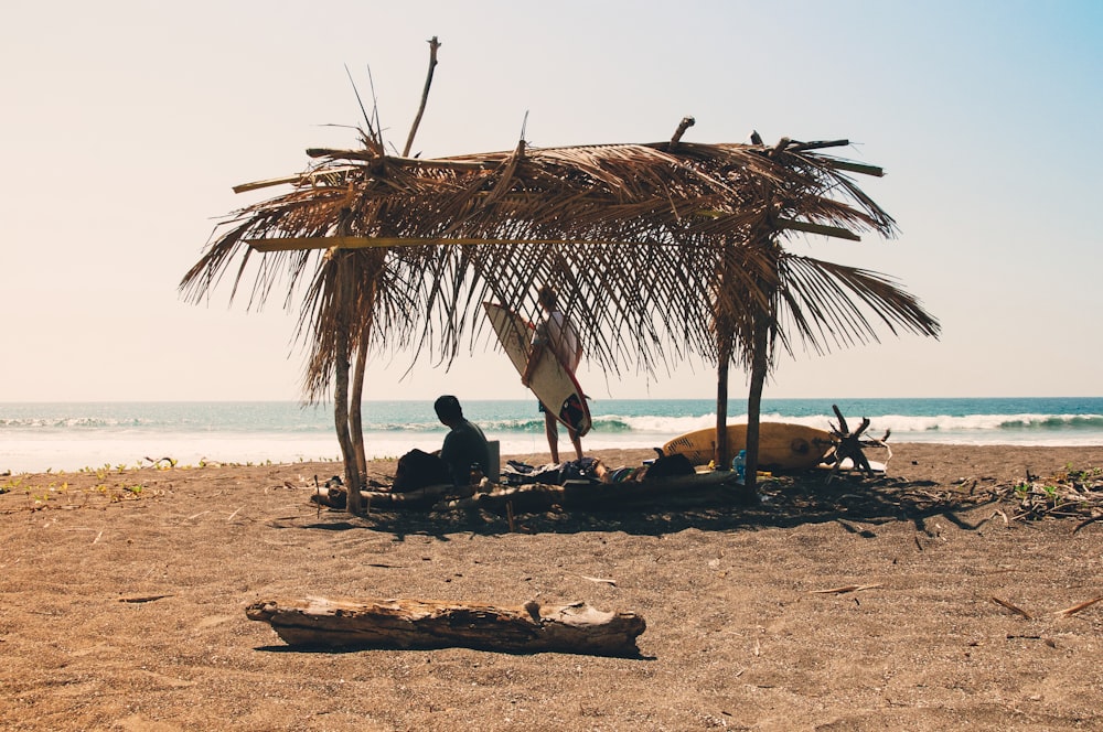man reclining under hut on seashore