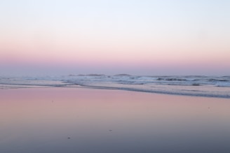 A serene beach at sunset with aqua waters and soft beige sands.