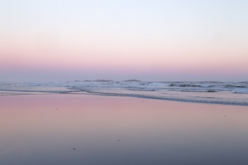 A serene beach at sunset with aqua waters and soft beige sands.