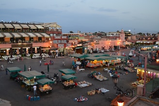 A lively community square with people of all ages sharing moments on colorful benches and market stalls.
