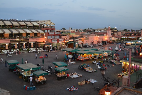 A lively village square with people enjoying outdoor seating near quaint shops and market stalls.