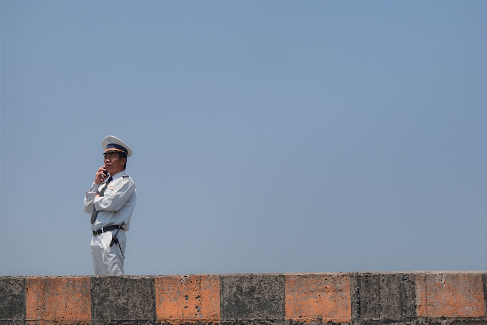 man in white long sleeve shirt and pants sitting on brown concrete wall during daytime