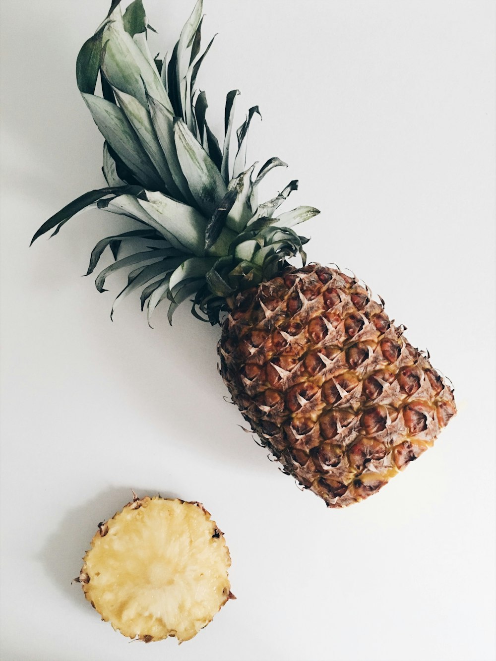 A pineapple lying on its side with its bottom sliced off.