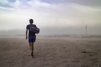 man wearing black t-shirt and blue short carrying black duffel bag on shoulder in the middle of desert
