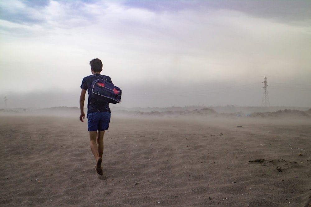 man wearing black t-shirt and blue short carrying black duffel bag on shoulder in the middle of desert