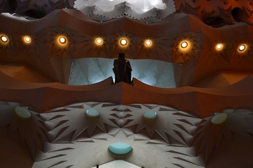 An abstract architectural design featuring pointed geometric patterns and circular light fixtures, creating a visually complex and textured surface. Soft, indirect lighting enhances the intricate details of the structure.