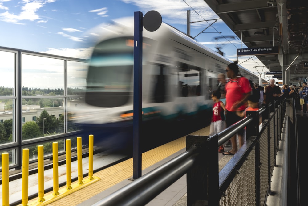 people standing on platform near blue and white train during daytime