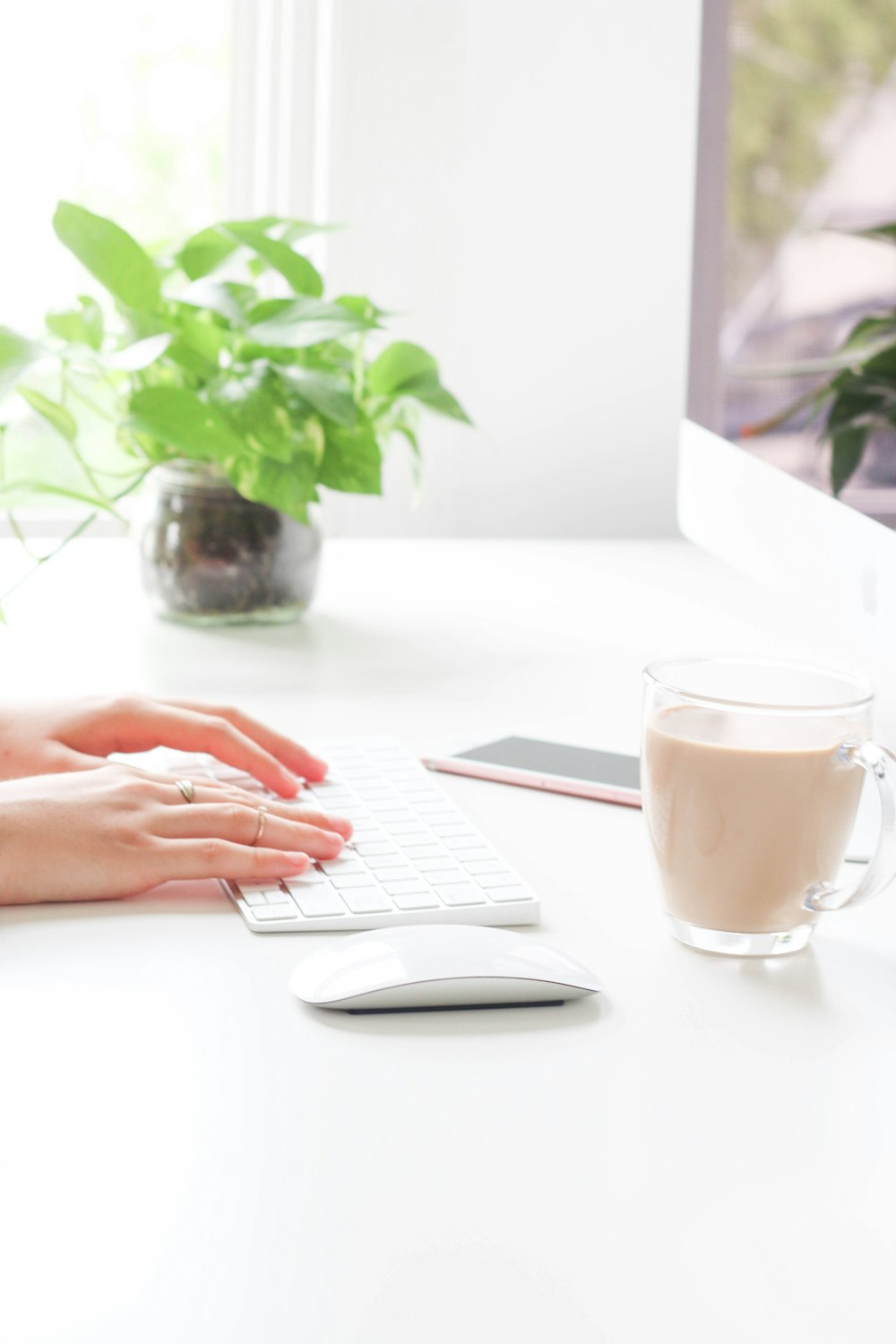 person using Apple Wireless Keyboard near Apple Magic Mouse, mug, and rose gold iPhone 6s on table