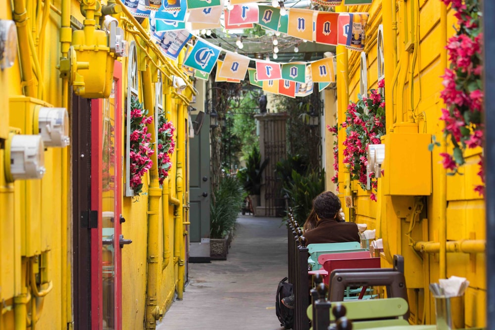 person in brown top sitting besides yellow building in pathway during daytime