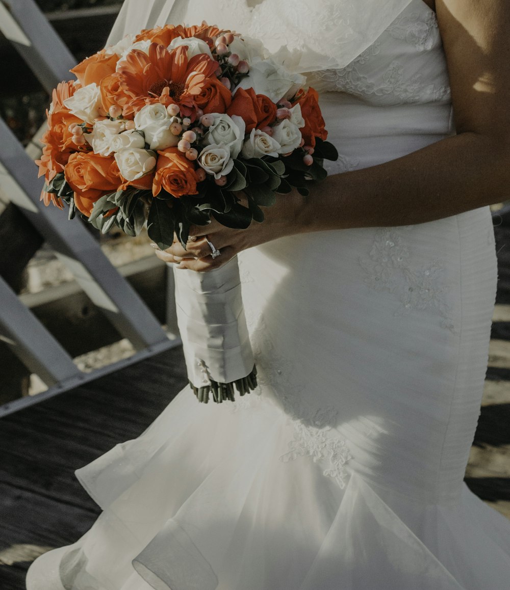 Mujer con vestido de novia blanco sosteniendo ramo de flores rojas y blancas