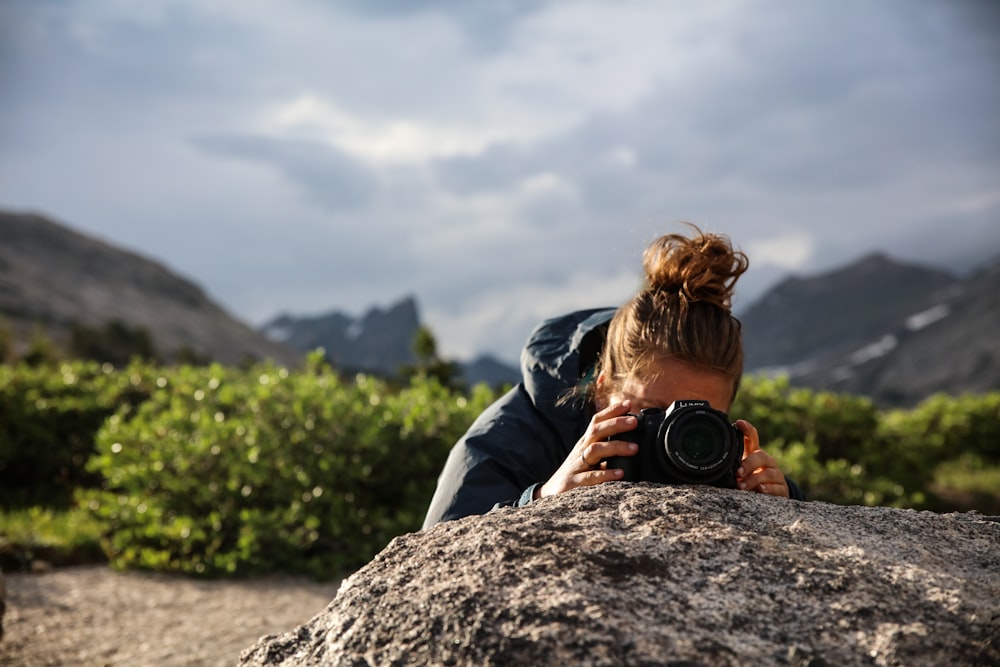 man in black jacket and blue denim jeans sitting on rock during daytime