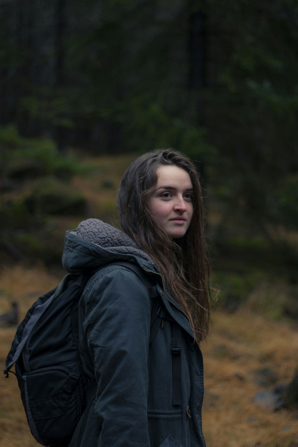 tilt-shift photography of woman wearing black backpack surrounded by green leafed trees