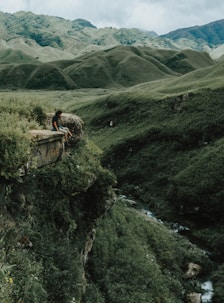 man sitting on brown rock on cliff with distance to mountains