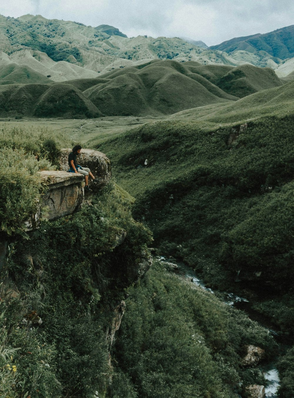 山までの距離と崖の上の茶色の岩の上に座っている男