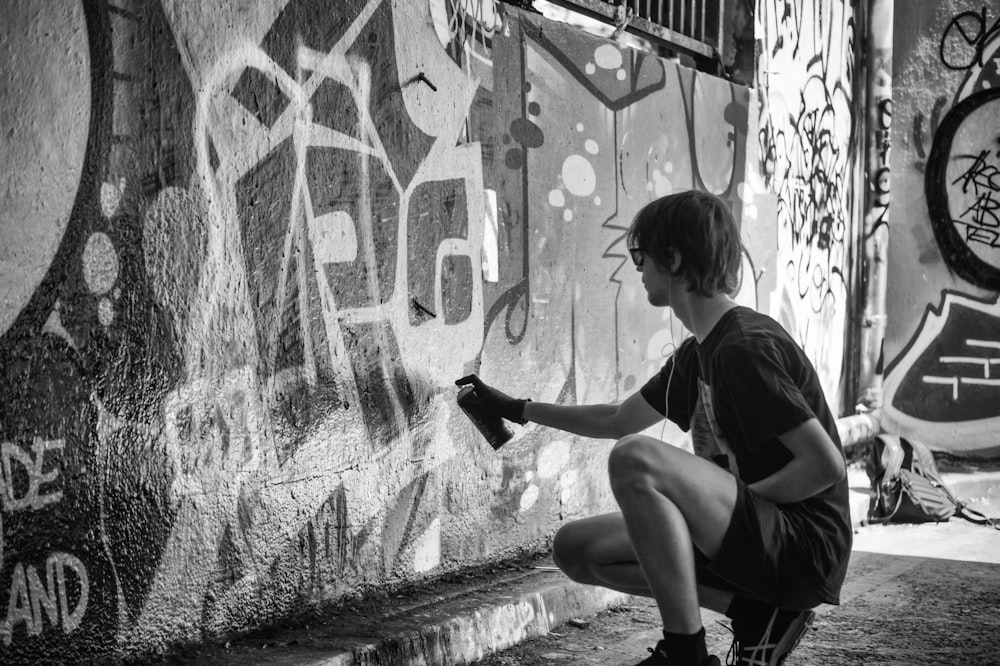 Photographie en niveaux de gris d’un homme vandalisant le mur pendant la journée