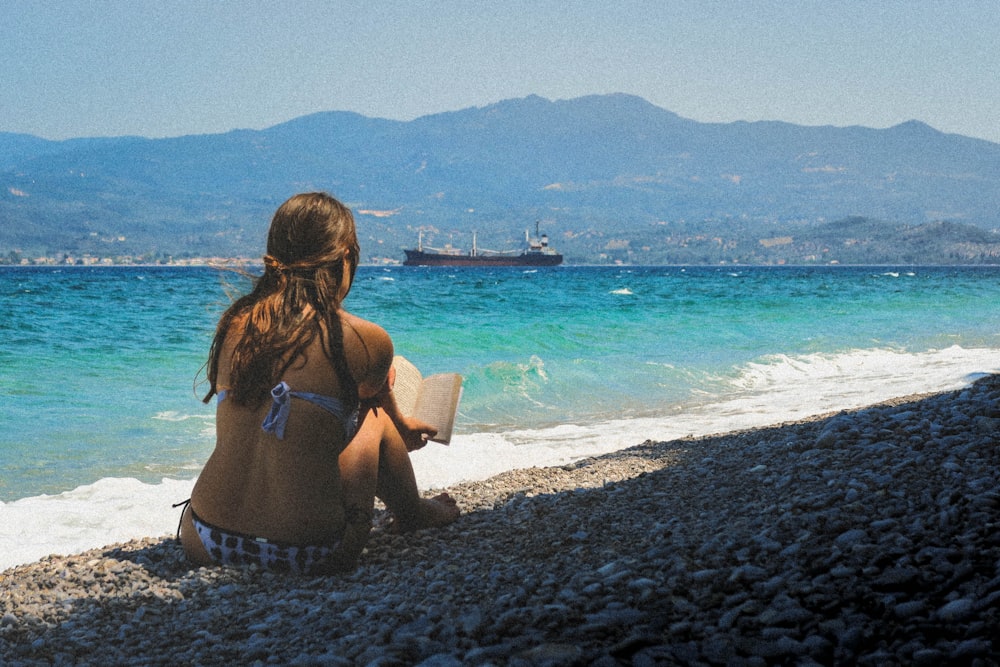 Donna seduta in riva al mare che legge il libro durante il giorno