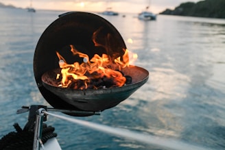 round black fire pit with charcoal on it burning beside calm body of water