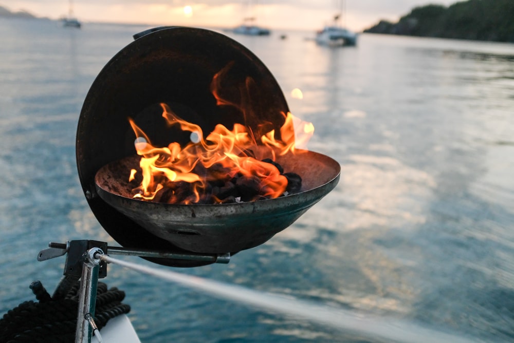 round black fire pit with charcoal on it burning beside calm body of water