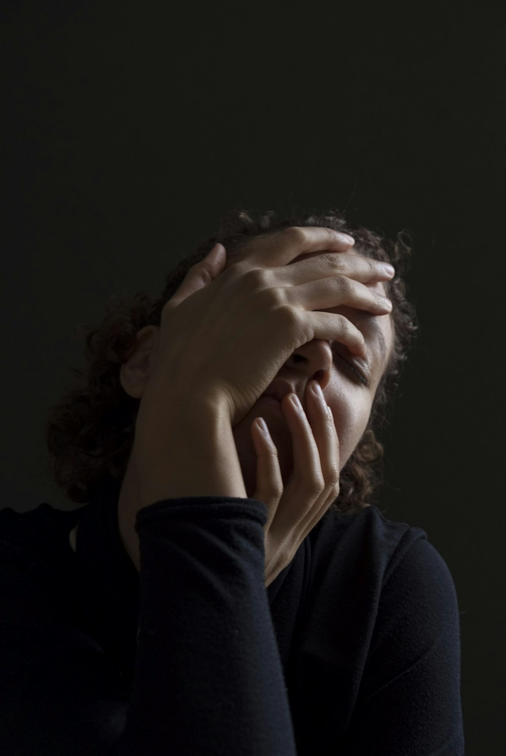 woman wearing blue long-sleeved shirt touching her face