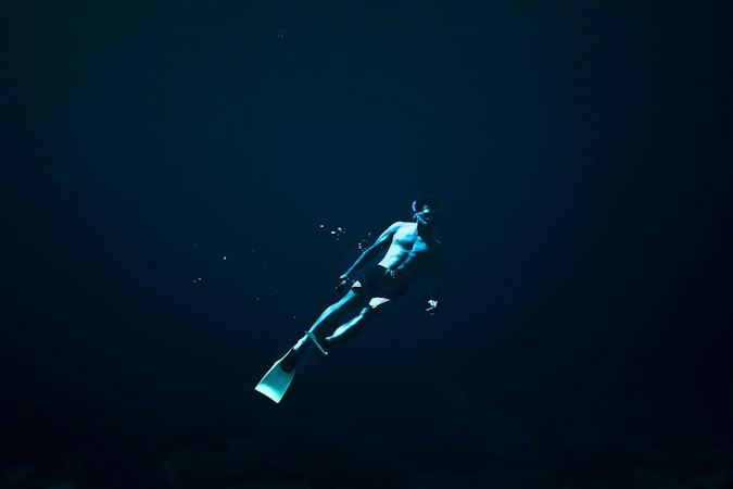 A freediver with long fins swimming alone through dark blue open water