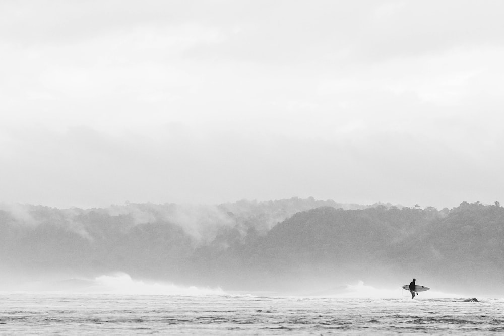 낮 사진 촬영 중 물 위에 서서 서핑 보드를 들고 있는 사람