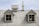 A weathered corrugated metal roof with two small dormer windows and a chimney. The windows have gray frames and are symmetrically placed. The roof exhibits signs of age and peeling paint.