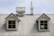 A weathered corrugated metal roof with two small dormer windows and a chimney. The windows have gray frames and are symmetrically placed. The roof exhibits signs of age and peeling paint.