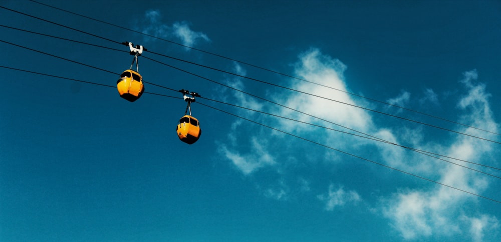 dois teleféricos amarelos movendo-se ao longo de um cabo durante o dia