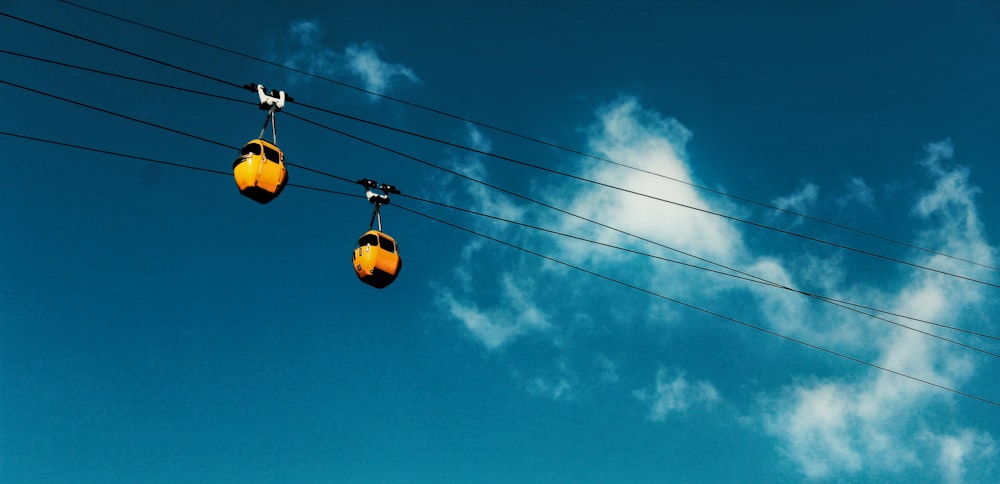 two yellow cable cars moving along a cable during day time
