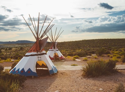 two white-blue-and-red teepee tents surrounded by green plants native teams background