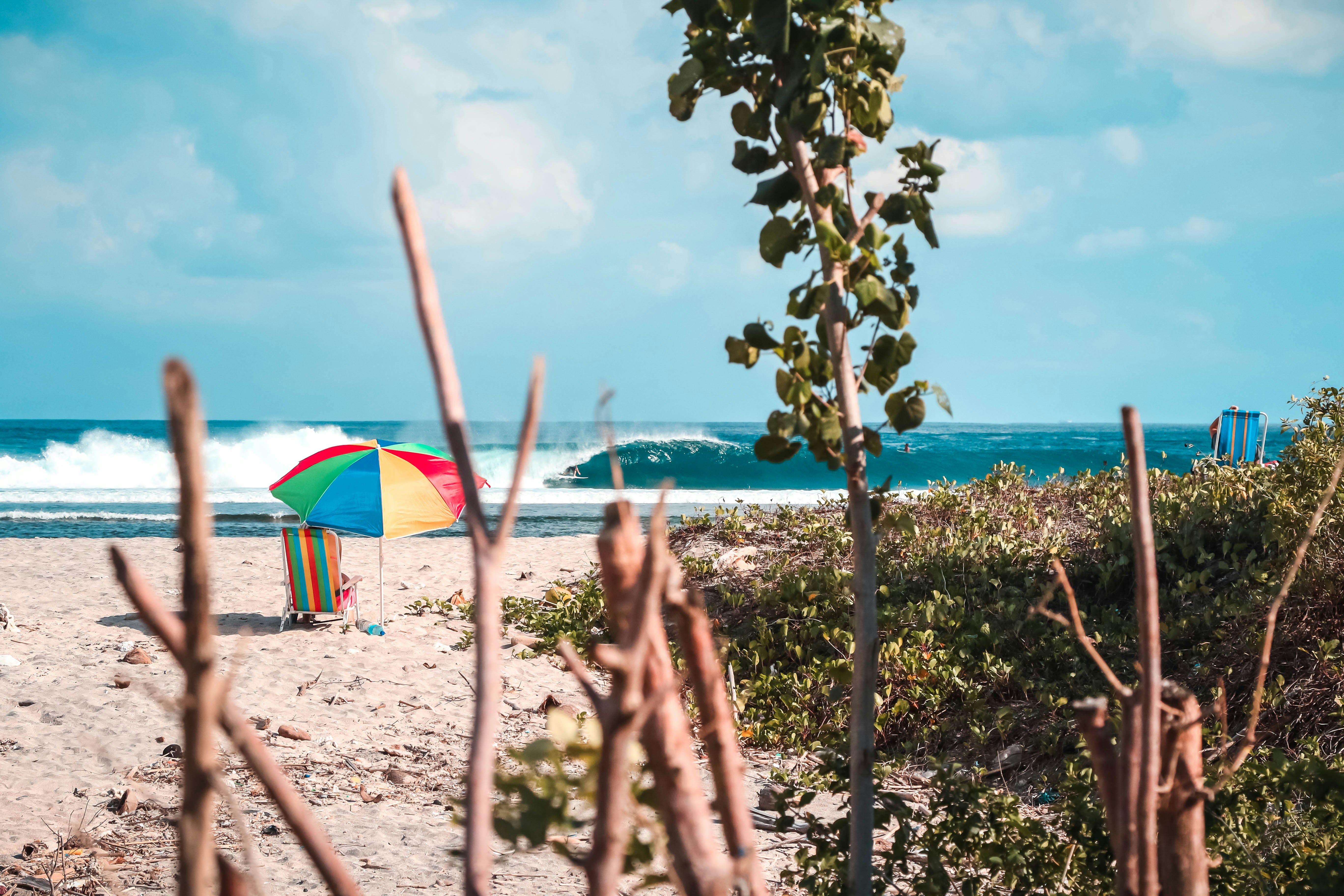red, yellow, blue, and green parasol on seashore, One of my favorite pictures from my travels to Indonesia. This break is hard to get to and in a remote village where surfers only come to when the swell is big.